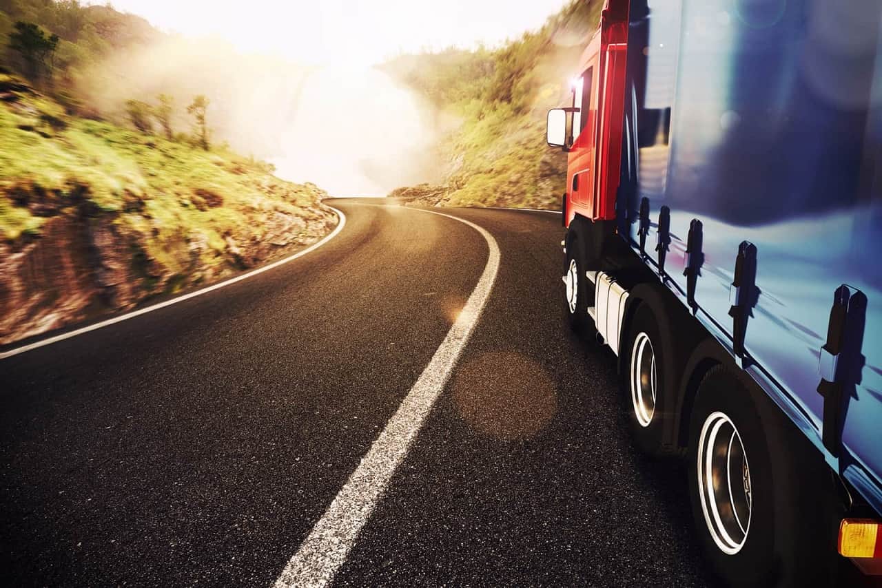 Transport międzynarodowy. Ciężarówka jadąca drogą lokalną w stronę słońca.